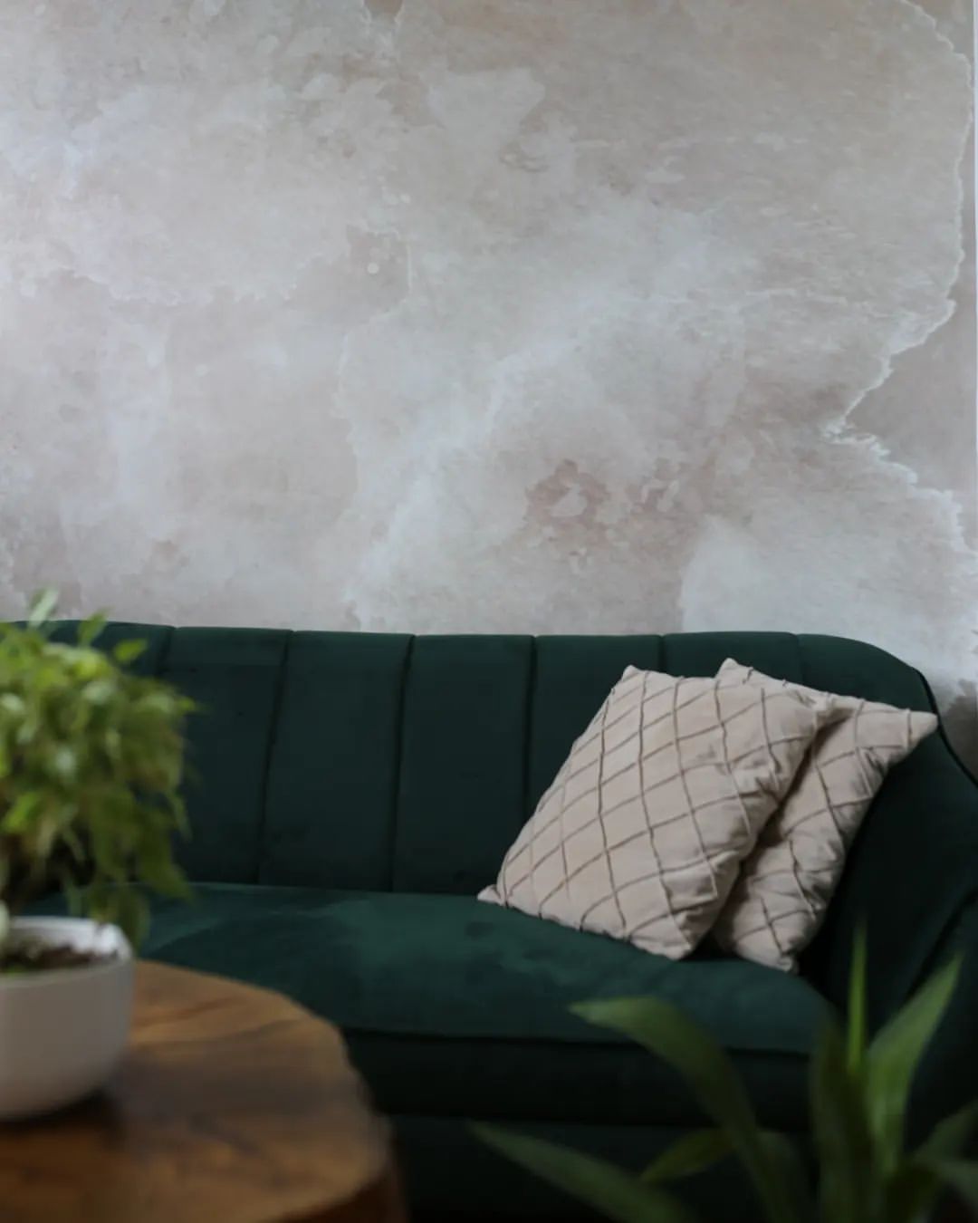 Interior con sofá de terciopelo verde, almohadas estampadas y pared con aspecto de mármol.