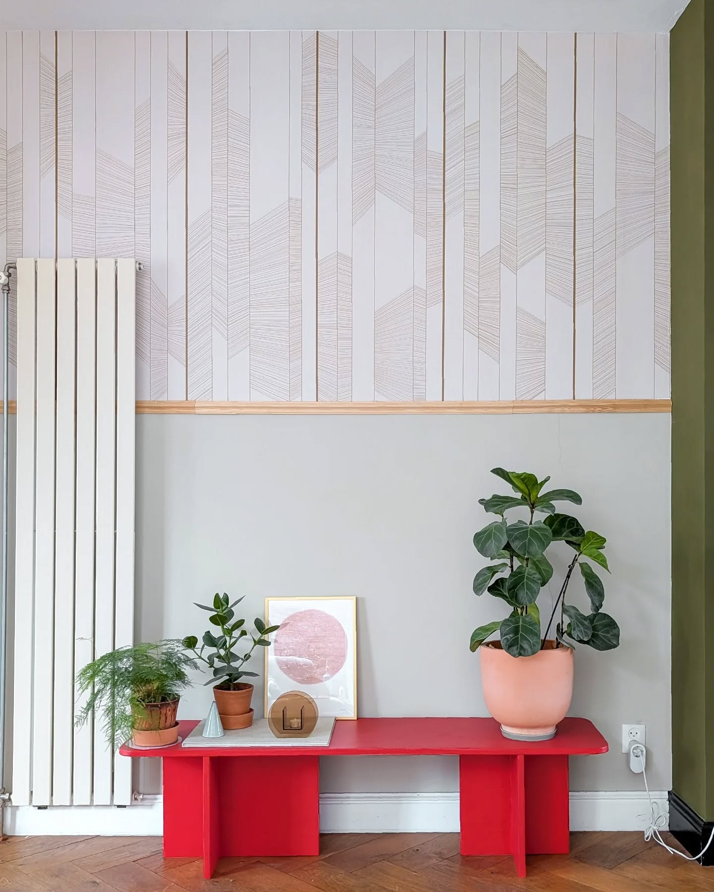 Interior con banco rojo, plantas y arte enmarcado contra una pared gris y blanca estampada.