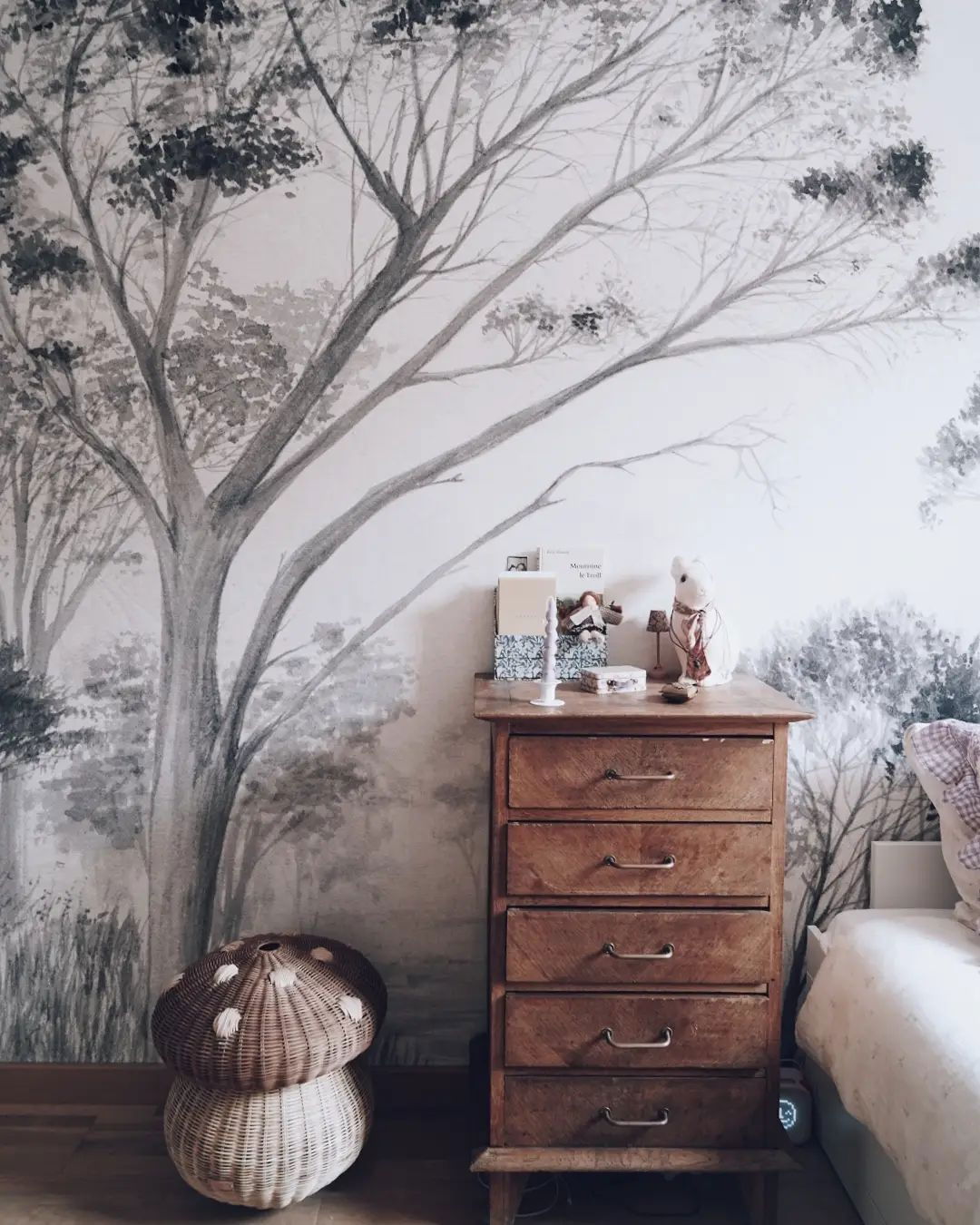 Chambre avec une murale de forêt, une commode en bois et un panier en osier en forme de champignon.