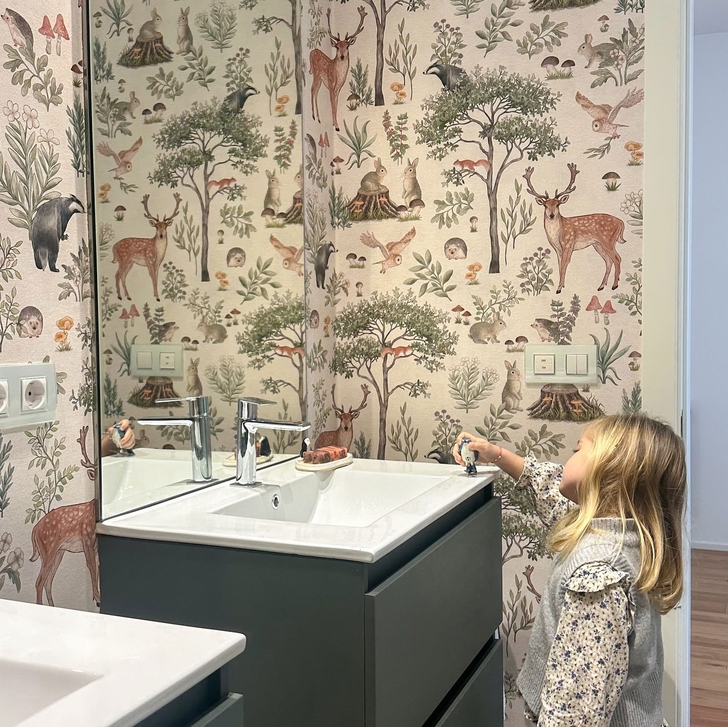 Bathroom with woodland-themed wallpaper and a child playing by the sink.