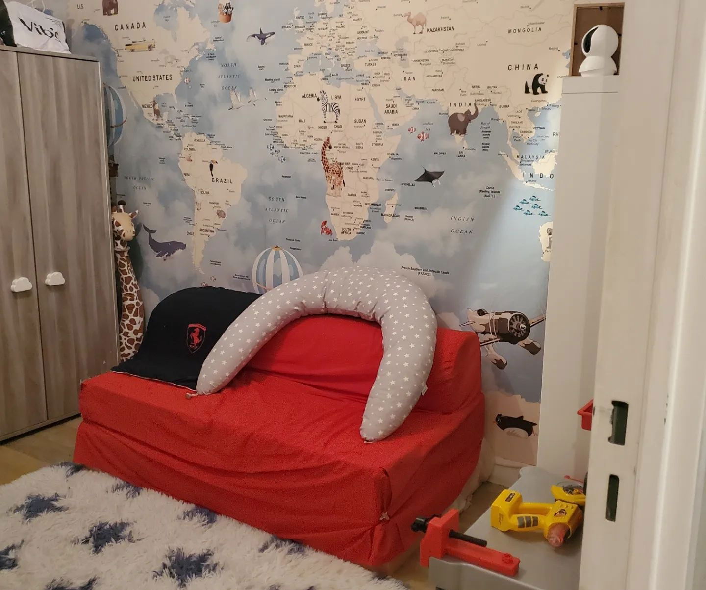Stanza di un bambino con carta da parati con mappa del mondo, divano rosso e peluche.
