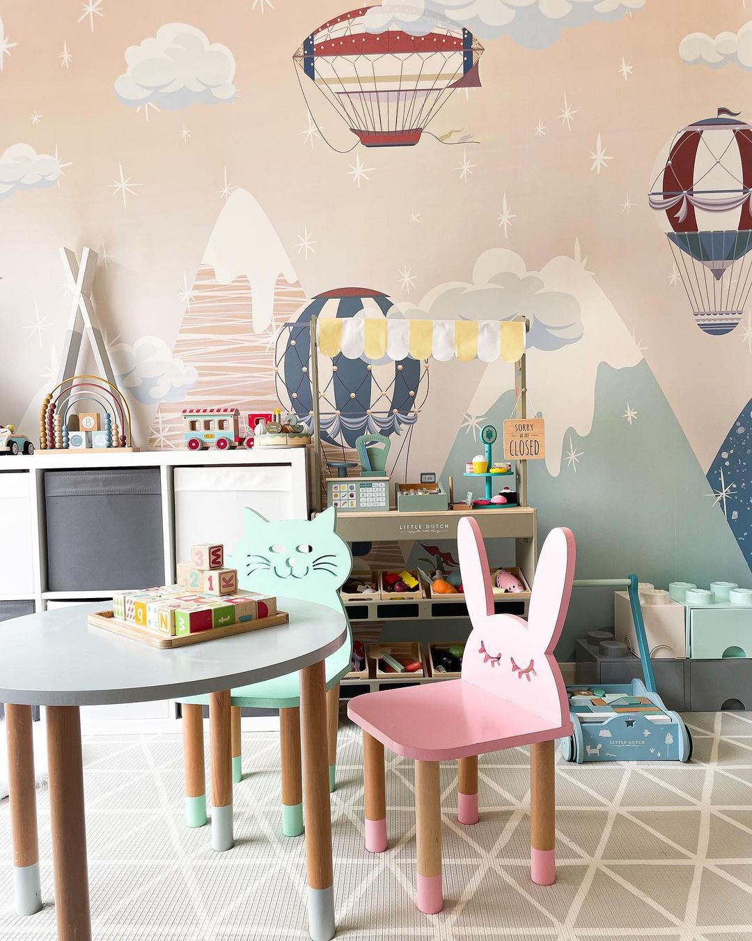 Playroom scene with Little Dutch market stand, cat and bunny chairs, round table with blocks, and hot air balloon wallpaper.
