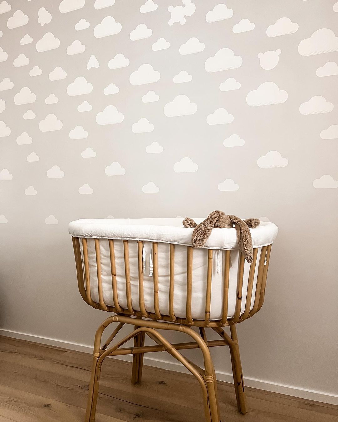 Baby-Stubenwagen aus Rattan mit weißer Wolkentapete. Stoffhase am Rand.