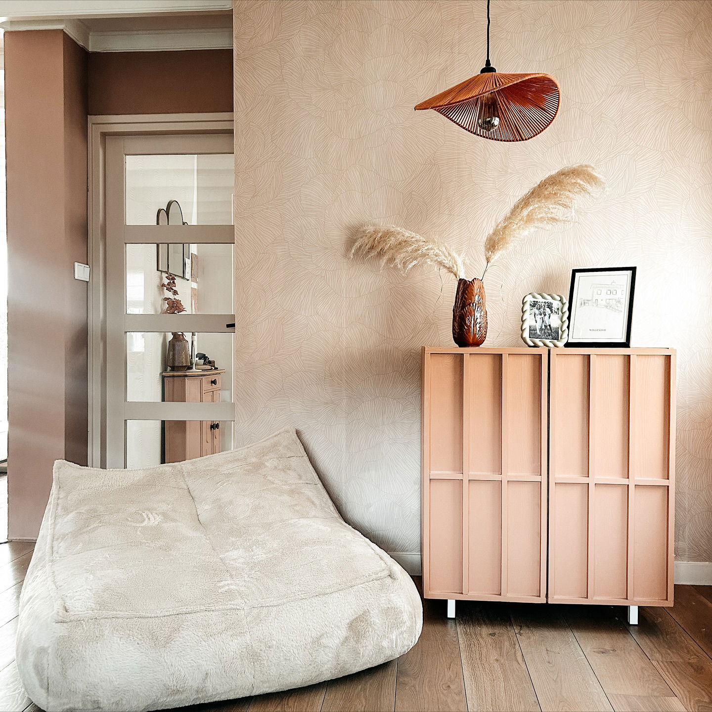 Cozy interior with cream beanbag, salmon cabinet, and pampas grass in vase.