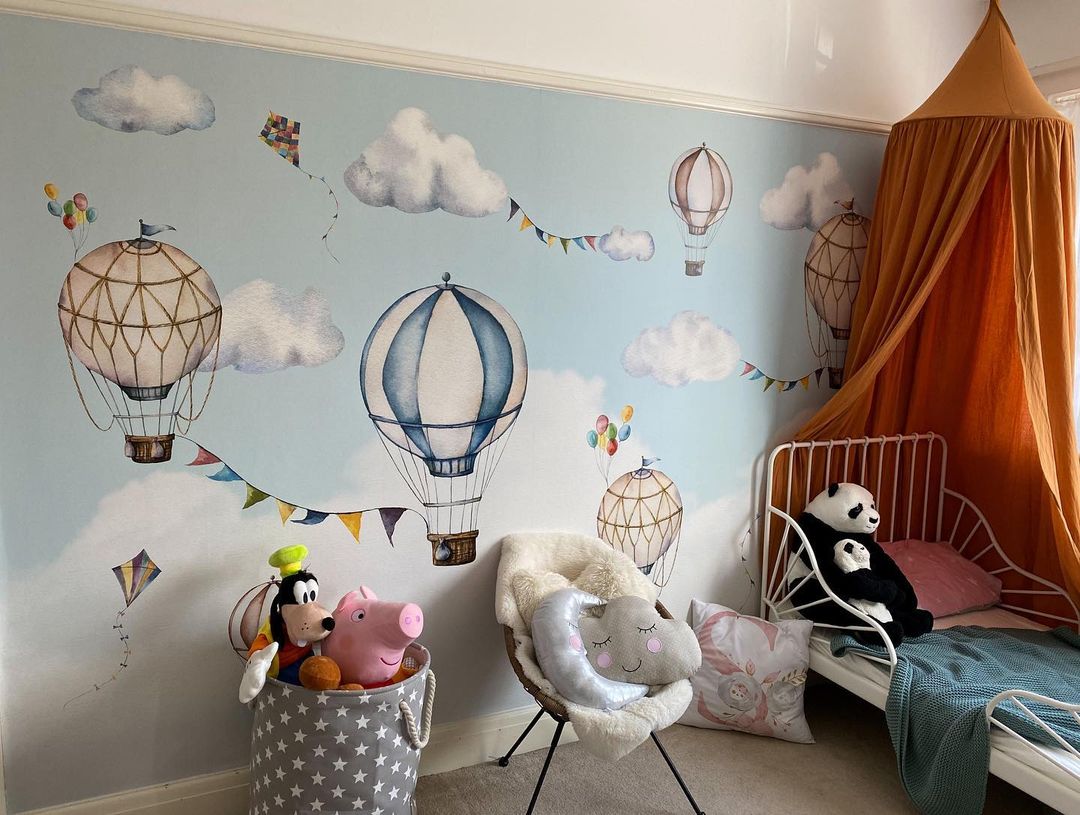 Chambre d'enfant avec papier peint de montgolfière, lit à baldaquin et animaux en peluche.