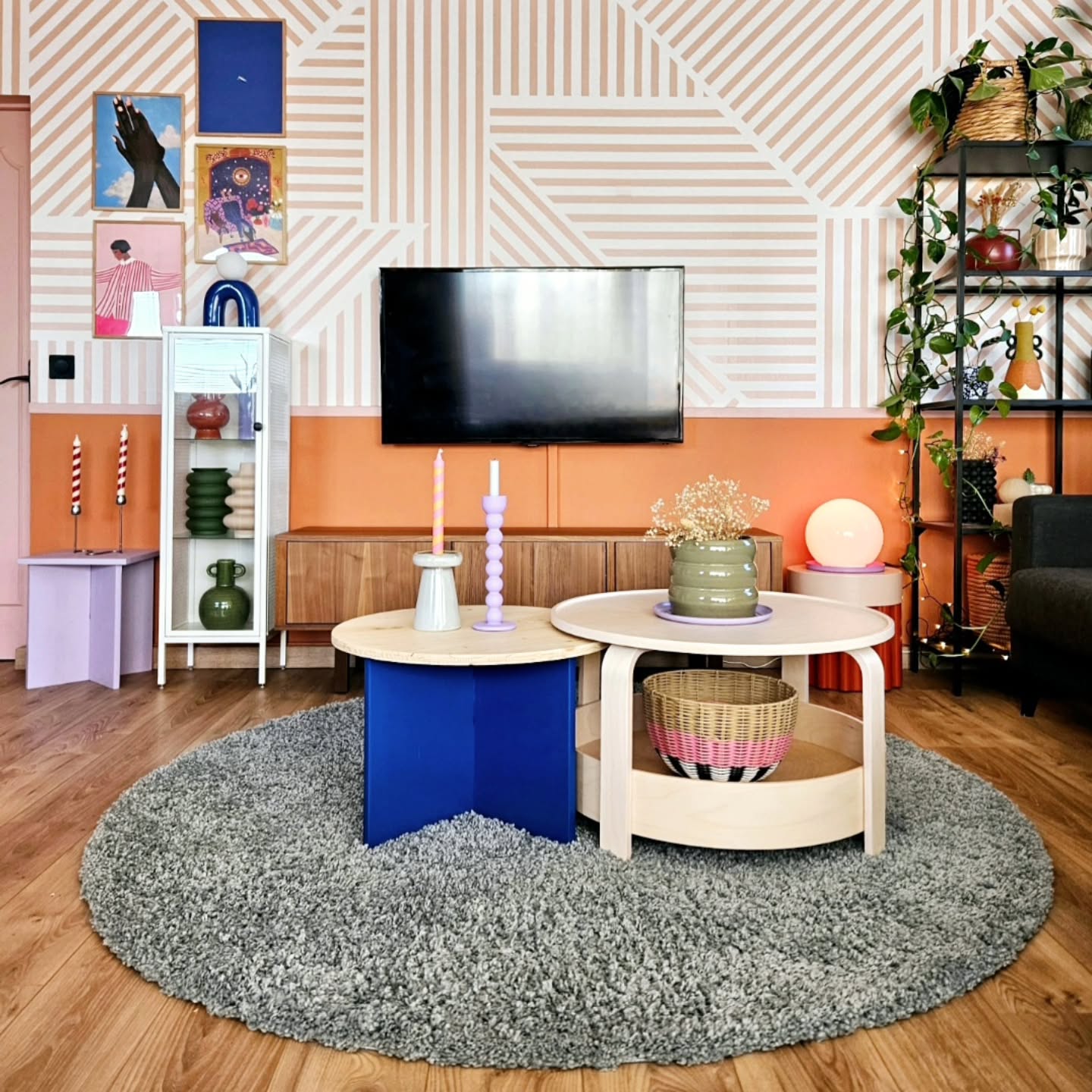 Living room with round gray rug, colorful tables, and geometric wall design.