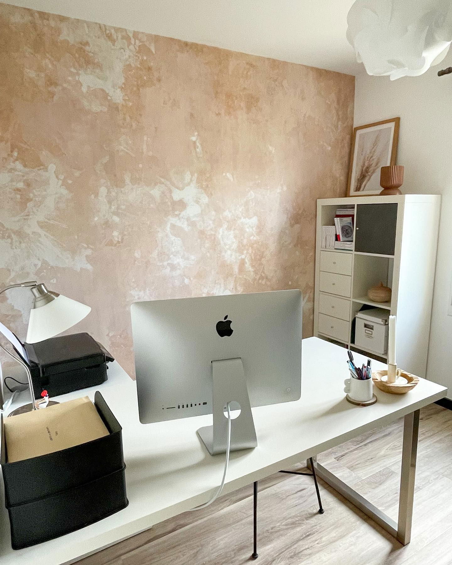 Homeoffice-Setup mit Apple iMac auf weißem Schreibtisch, schwarzen Organizern und dekorativer Wandstruktur.