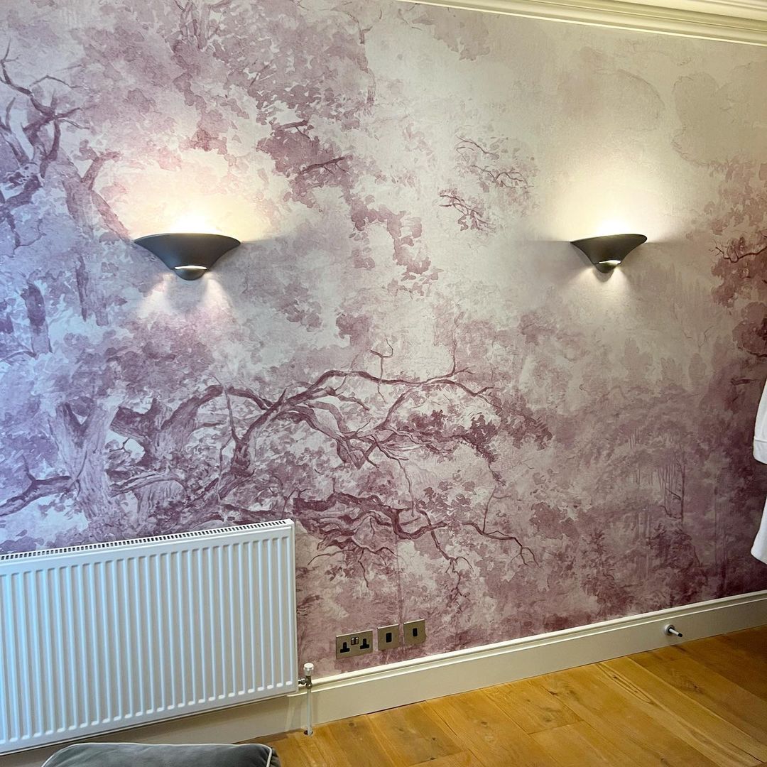 Mur intérieur avec papier peint arbre violet, éclairage des appliques, radiateur blanc et plancher en bois.
