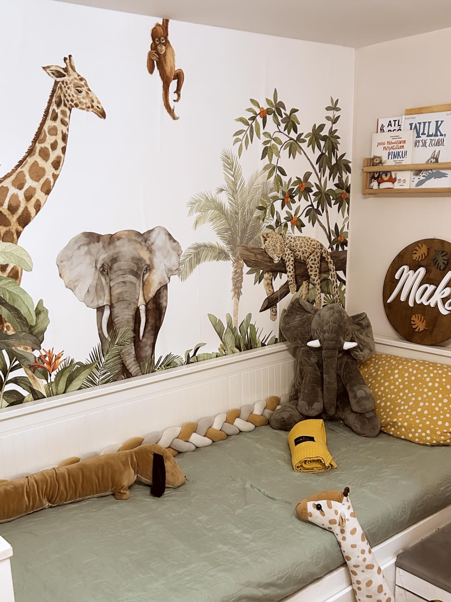 Child's room with jungle-themed wall decals and stuffed animals on a green bed.