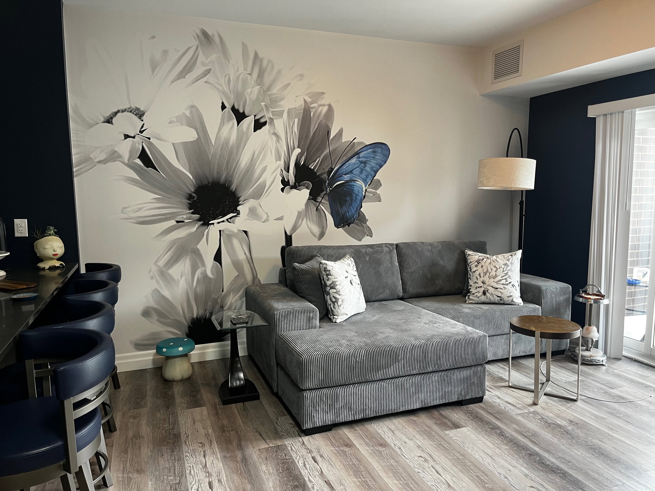 Graue Modul-Couch mit gemusterten Kissen vor einem Wandgemälde mit Gänseblümchen und einem blauen Schmetterling.