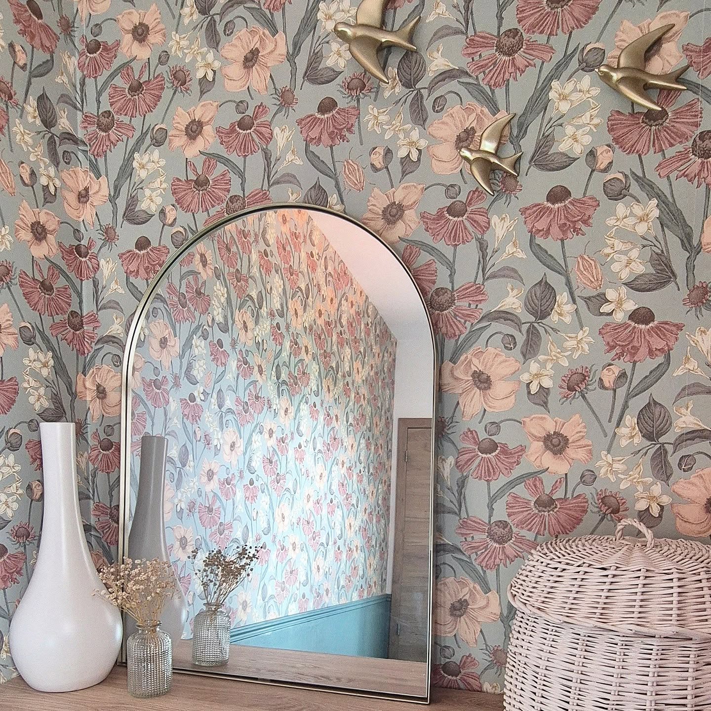 Interior with floral wallpaper, gold bird wall decor, and arched mirror reflecting a similar floral pattern.