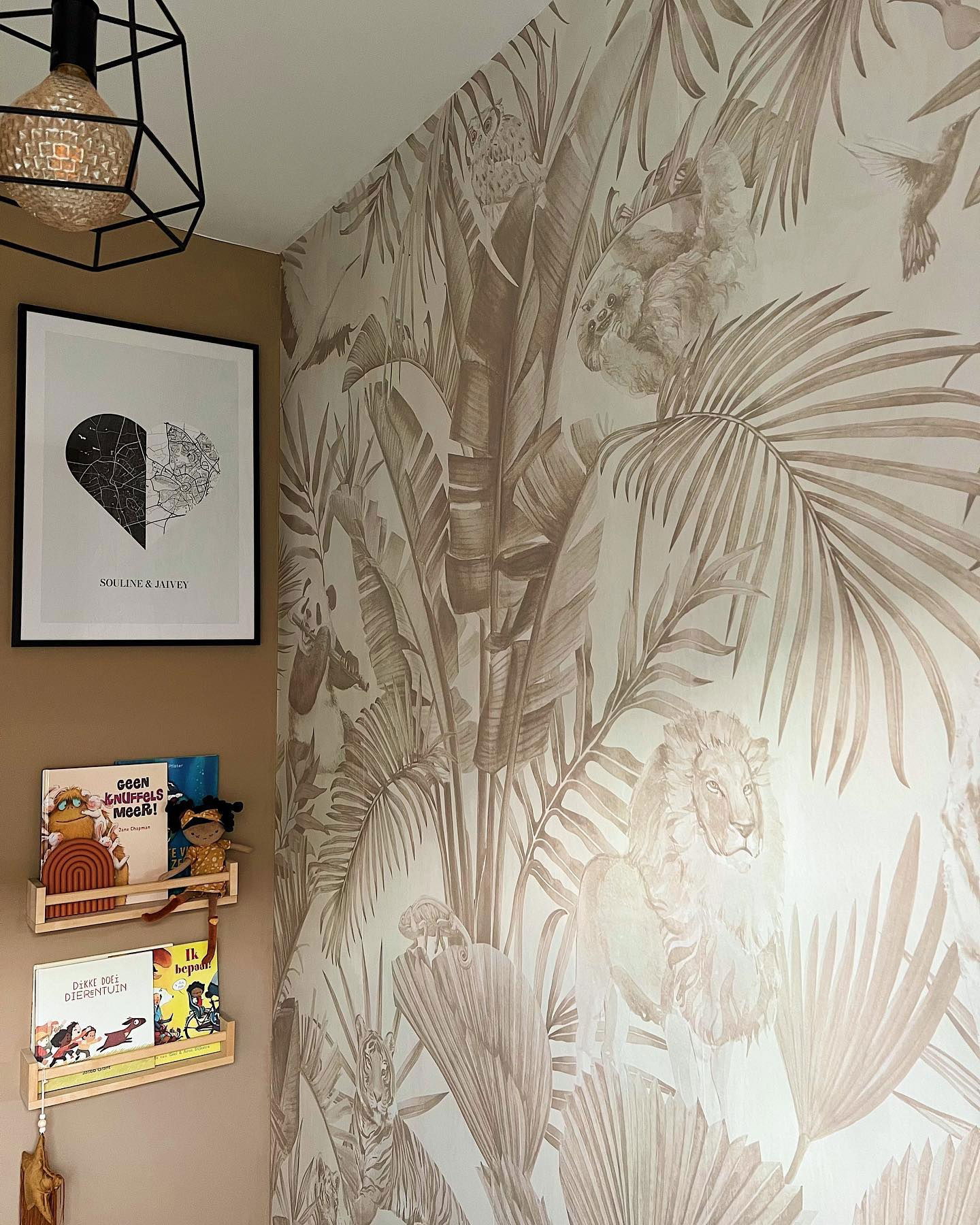 Coin de nurserie avec papier peint jungle, livres sur des étagères et carte de cœur encadrée.