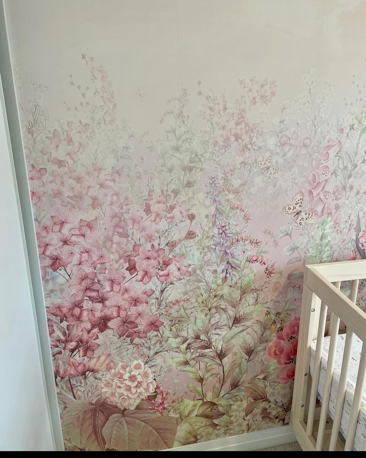 Muur van kinderkamer met roze bloemenbehang en witte wieg.