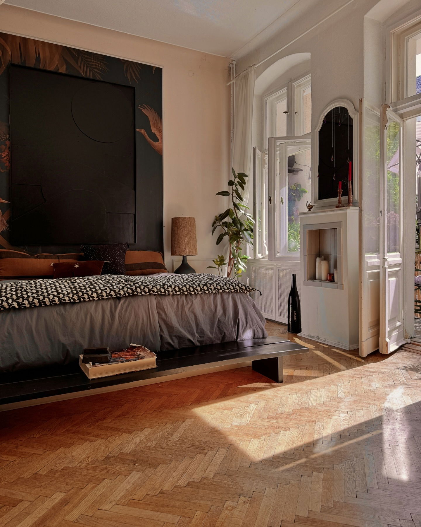Sonnendurchflutetes Schlafzimmer mit Parkettboden, Bett mit gemusterter Decke und offenen Türen.