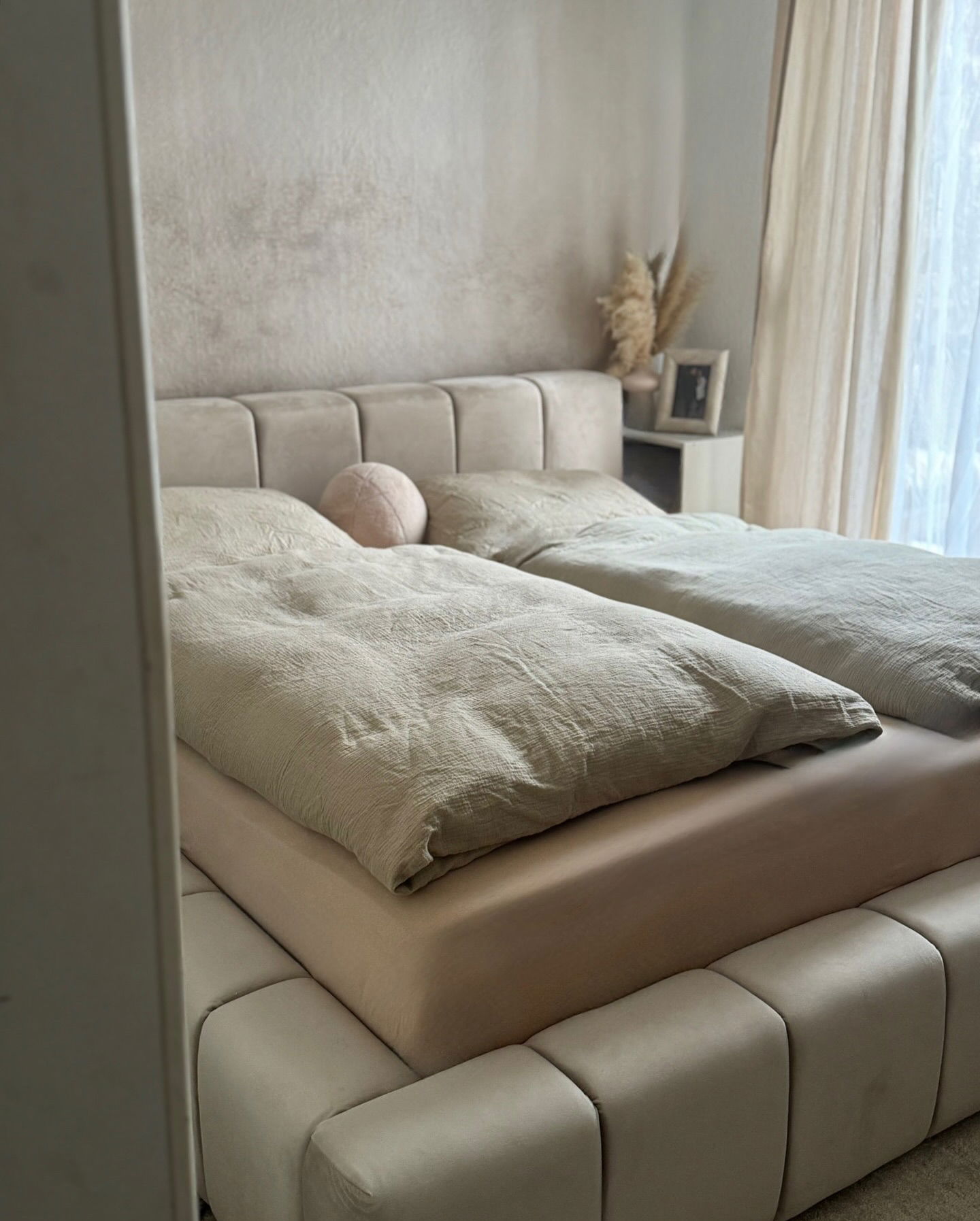 Beige polstret seng med linned sengetøj og en rund pude.