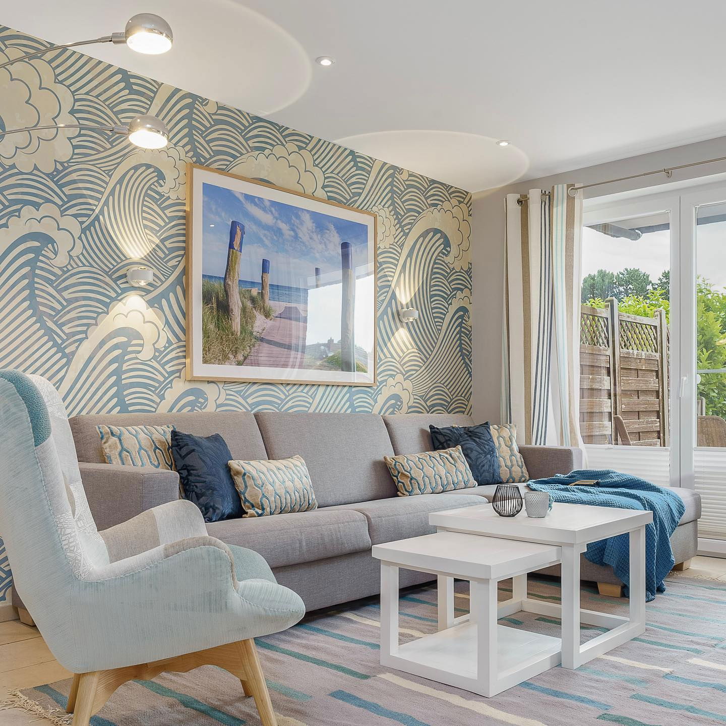 Living room with gray sofa, blue accents, wave-patterned wallpaper, and beach photo.