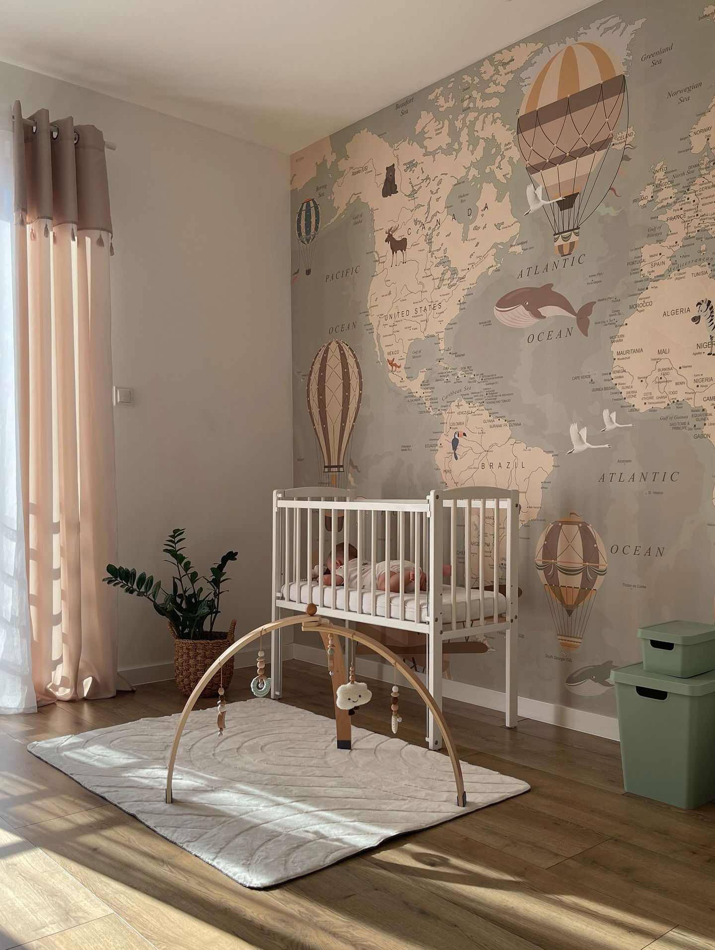 Nursery with white crib, wooden baby gym, and world map wallpaper with hot air balloons.
