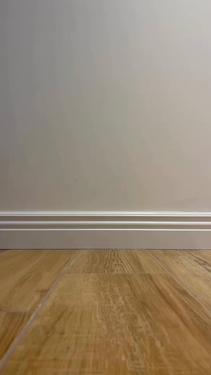 Interior shot of a room with light wood flooring and a white wall with base molding.