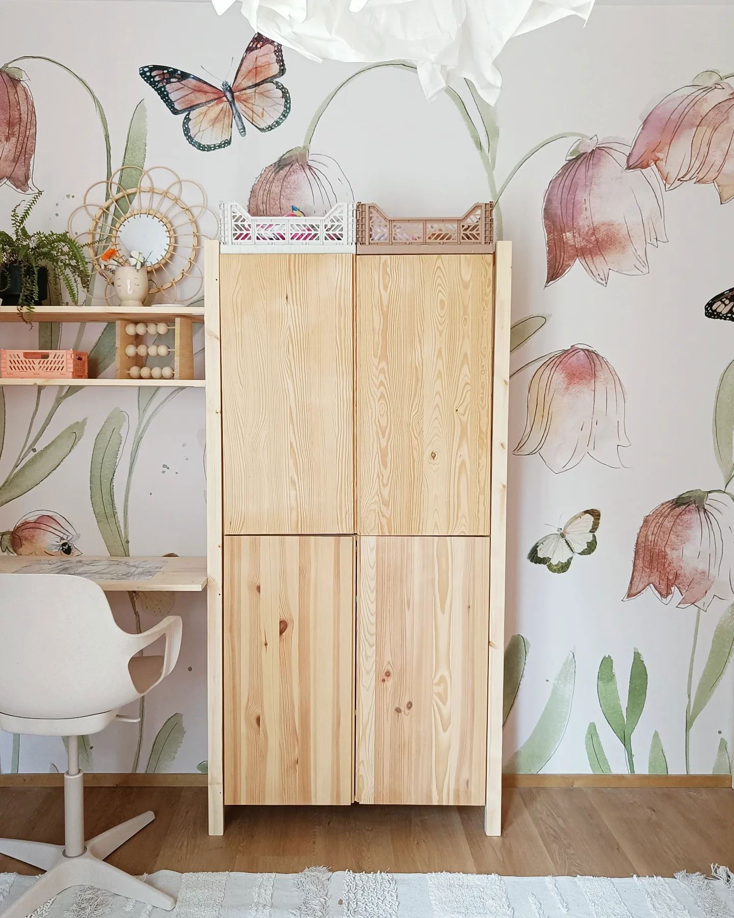 Child's room with light wood cabinet, desk, and floral wallpaper.