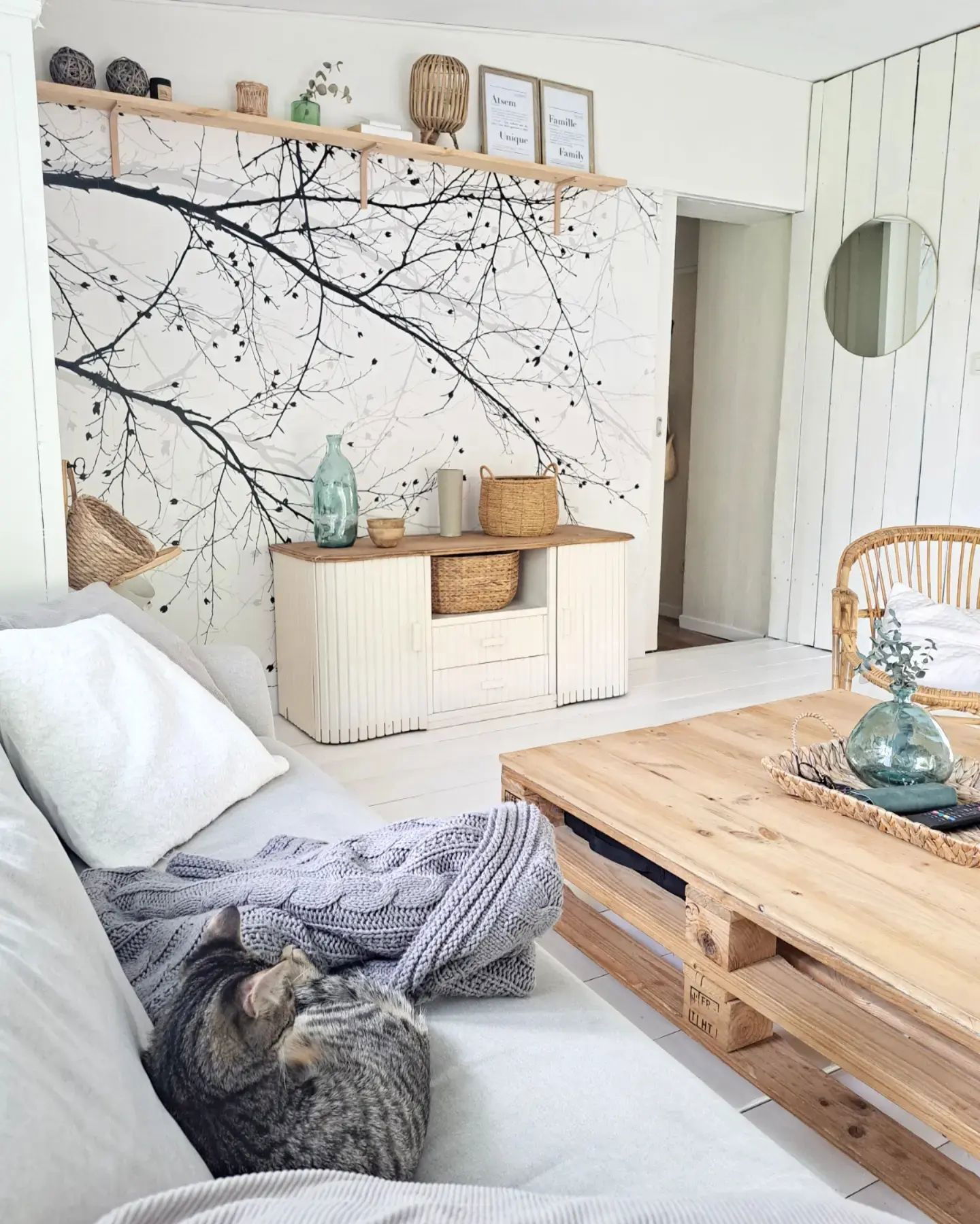 Cozy living room with sleeping tabby cat on sofa, pallet coffee table, and tree branch wall art.