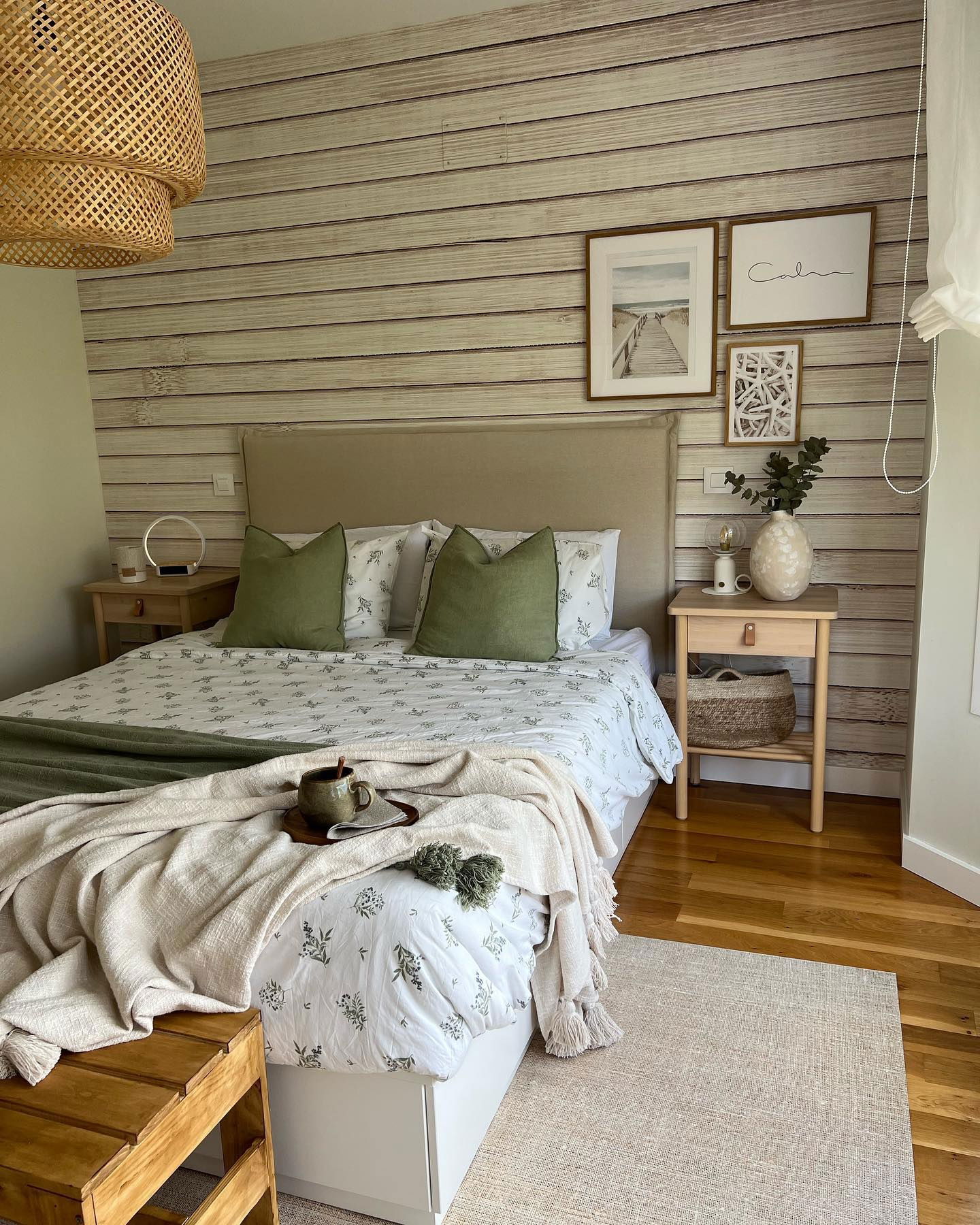 Cozy bedroom with wood-look wallpaper, neutral bedding with green accents, and woven pendant light.