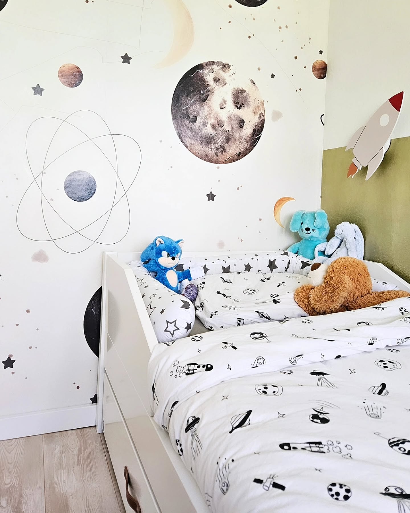 Kinderzimmer mit Weltraumtapete, weißem Bett und Stofftieren.