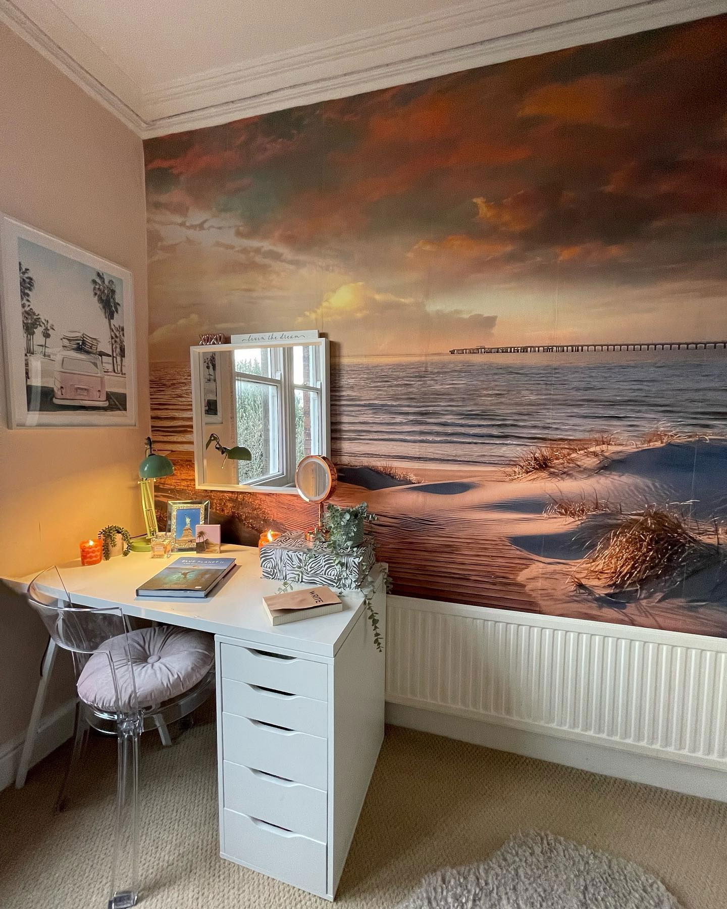 Home office setup with white desk, clear chair, and beach scene wallpaper.