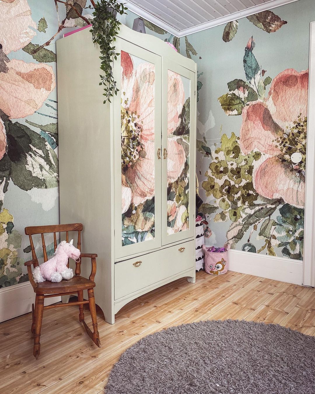 Kinderzimmer mit Blumentapete, salvigrünem Kleiderschrank und Holzstuhl mit rosa Einhorn.