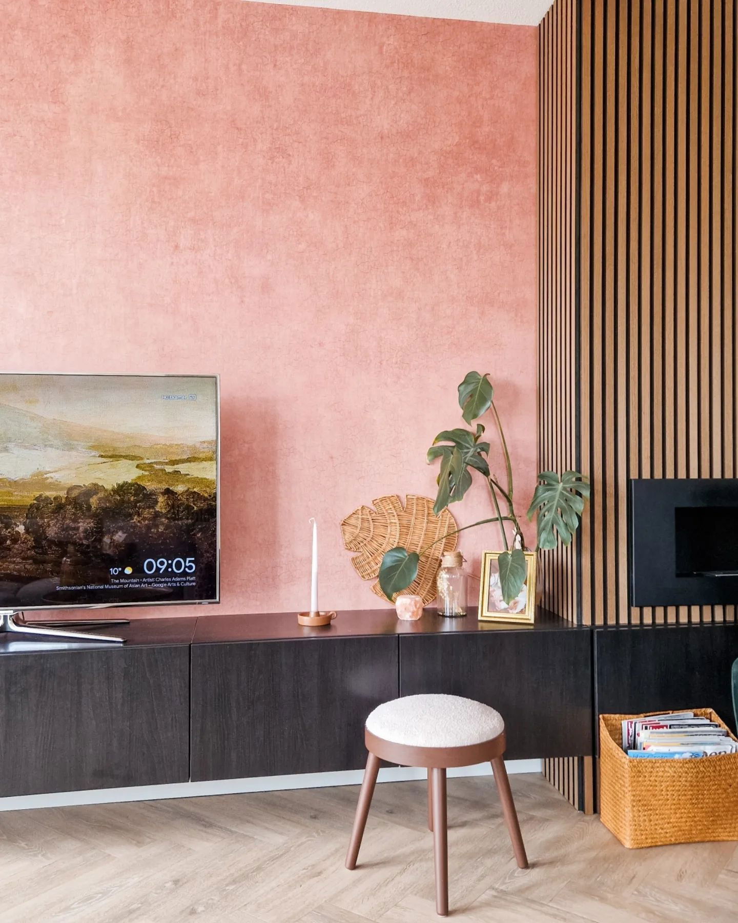 Living room with pink textured wall, wood slat accent, and dark wood media console with TV and decor.