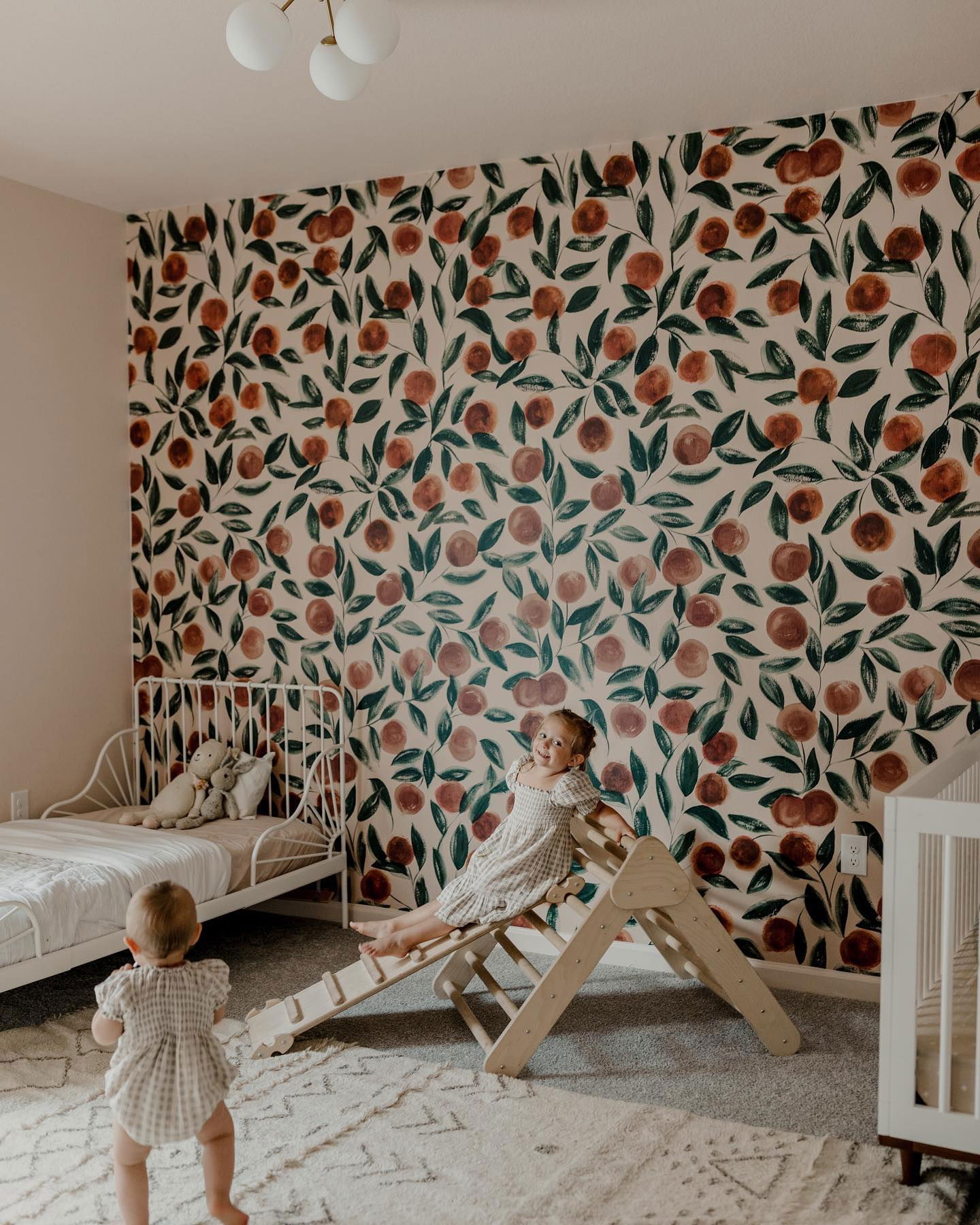 Nursery with orange floral wallpaper, white crib, and wooden climbing toy.