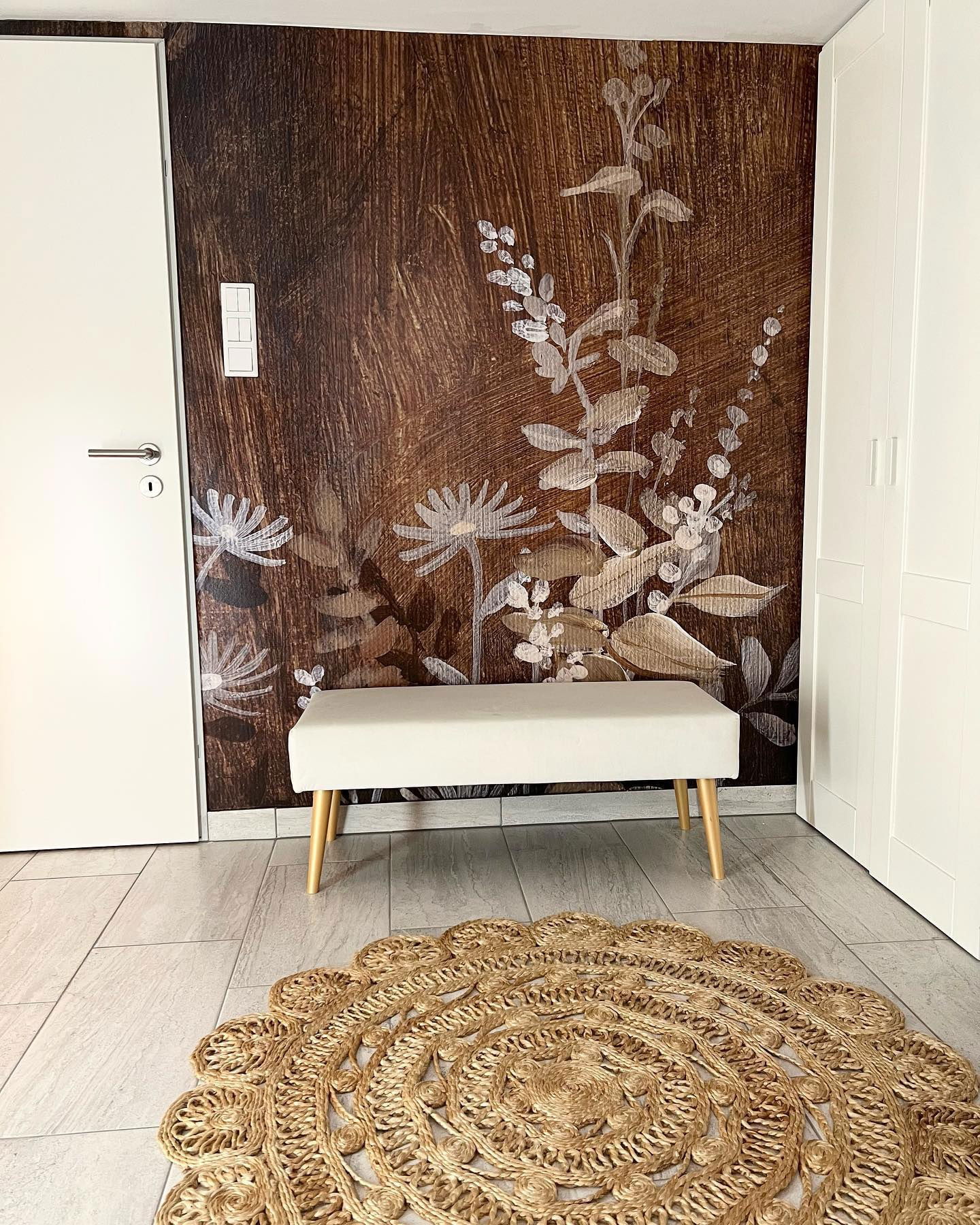 Hallway with floral wallpaper, white bench with wood legs, and round jute rug.