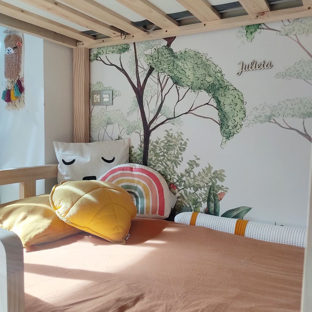 Child's bed with tree wallpaper, "Julieta" name art, and decorative pillows.