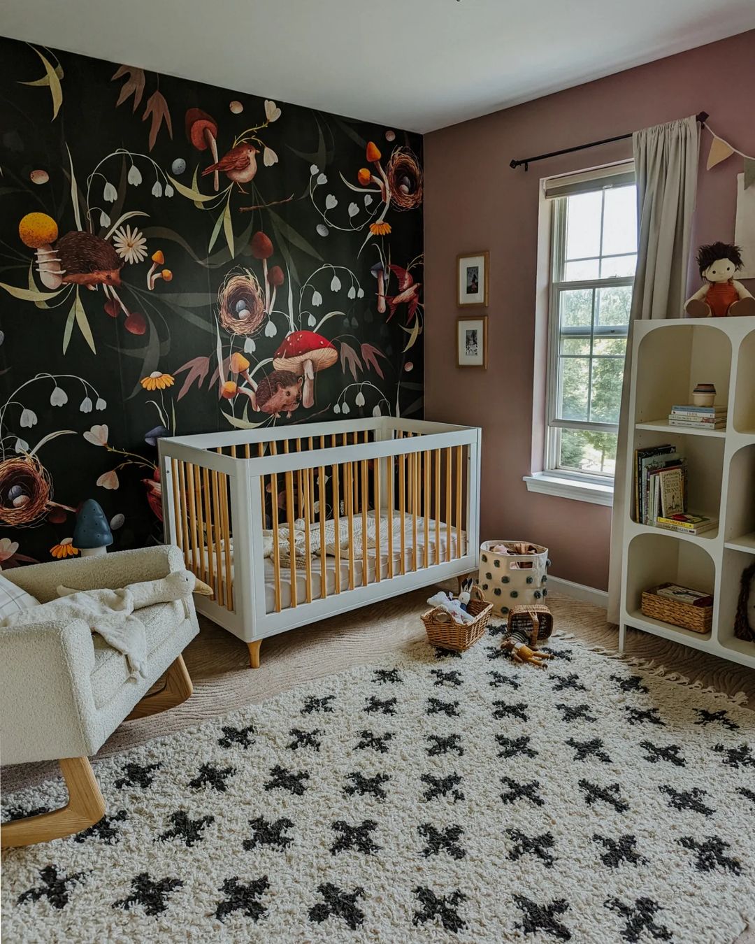 Kinderzimmer mit weißer Wiege vor Blumentapete, Schaukelstuhl und gemustertem Teppich.
