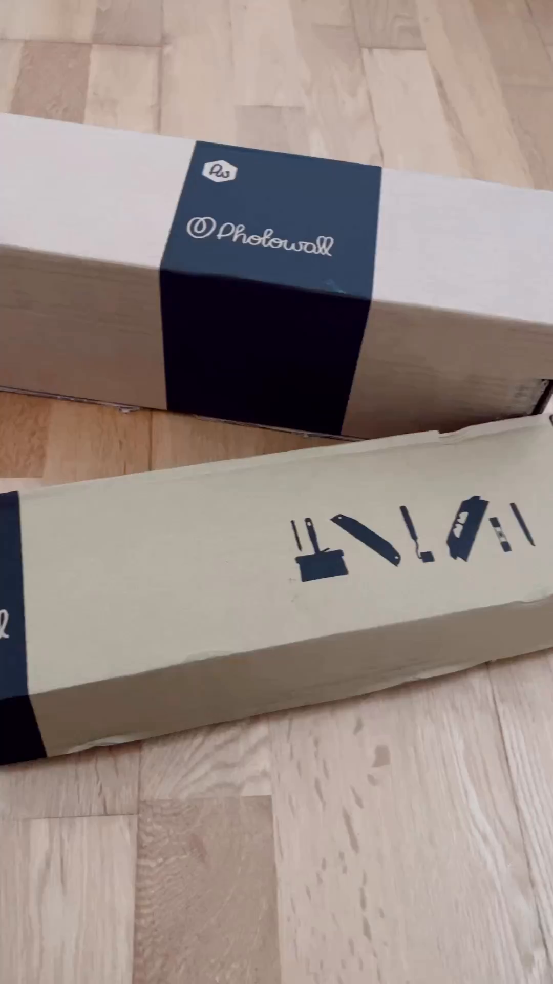Two Photowall boxes on a wood floor, one with installation tool icons.