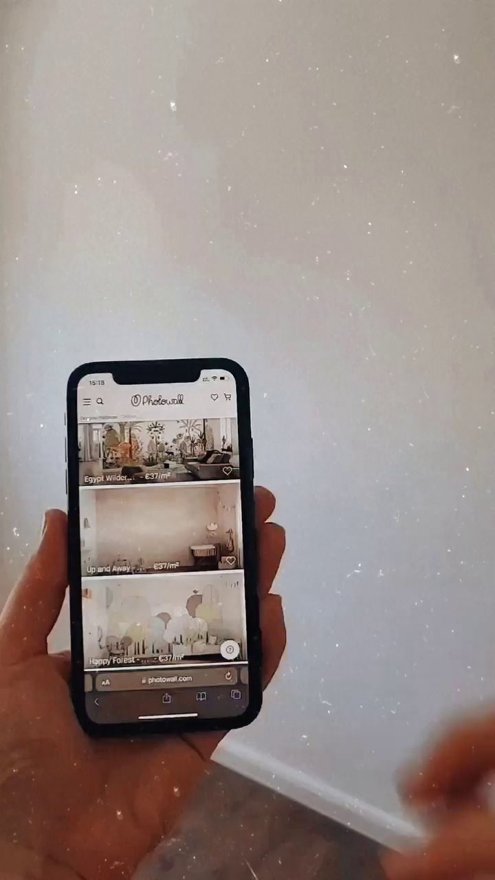 Hand holding a phone displaying the Photowall website, showcasing wallpaper designs.