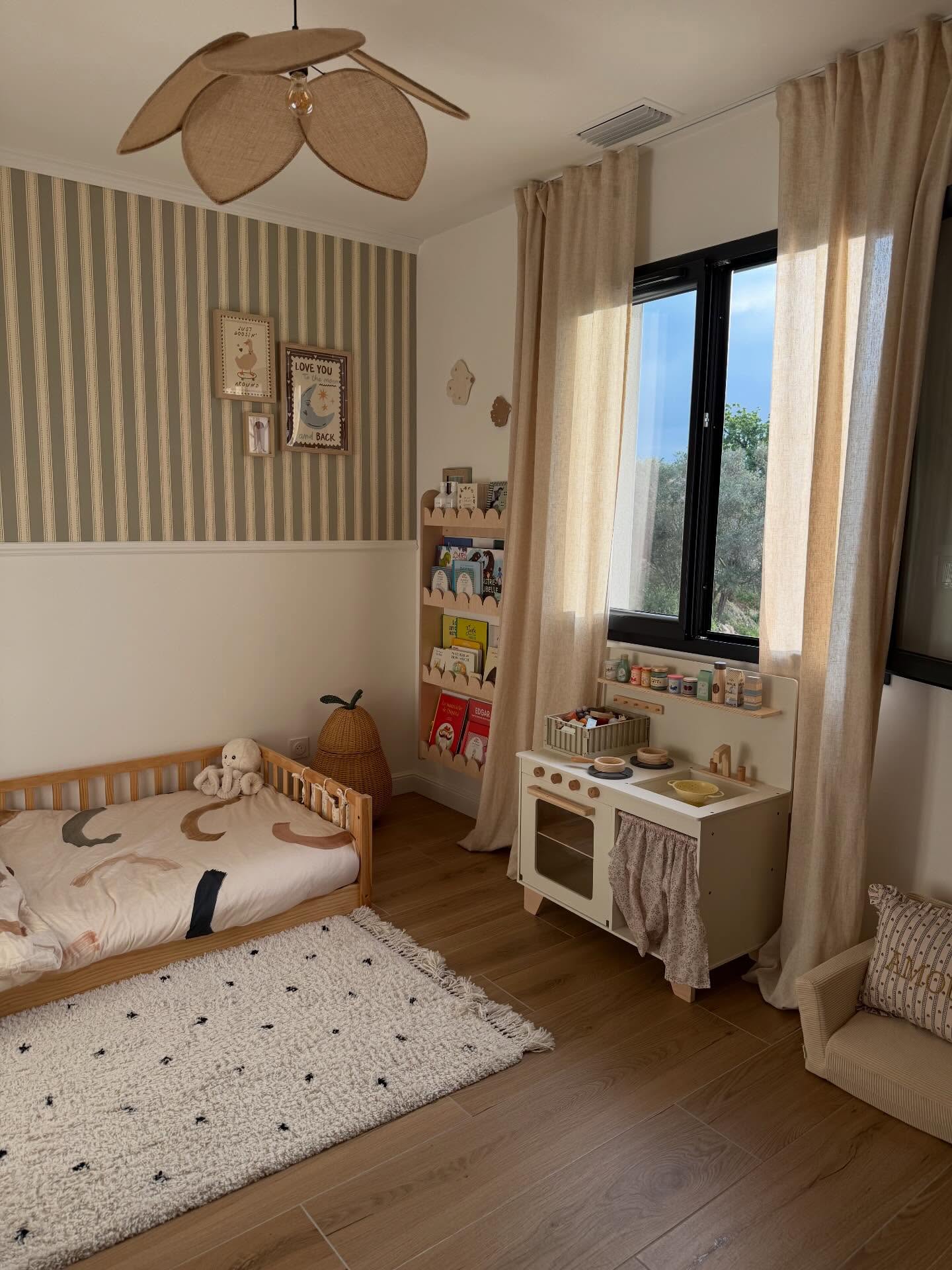 Children's bedroom with a toy kitchen, bed, bookshelf, and fan.