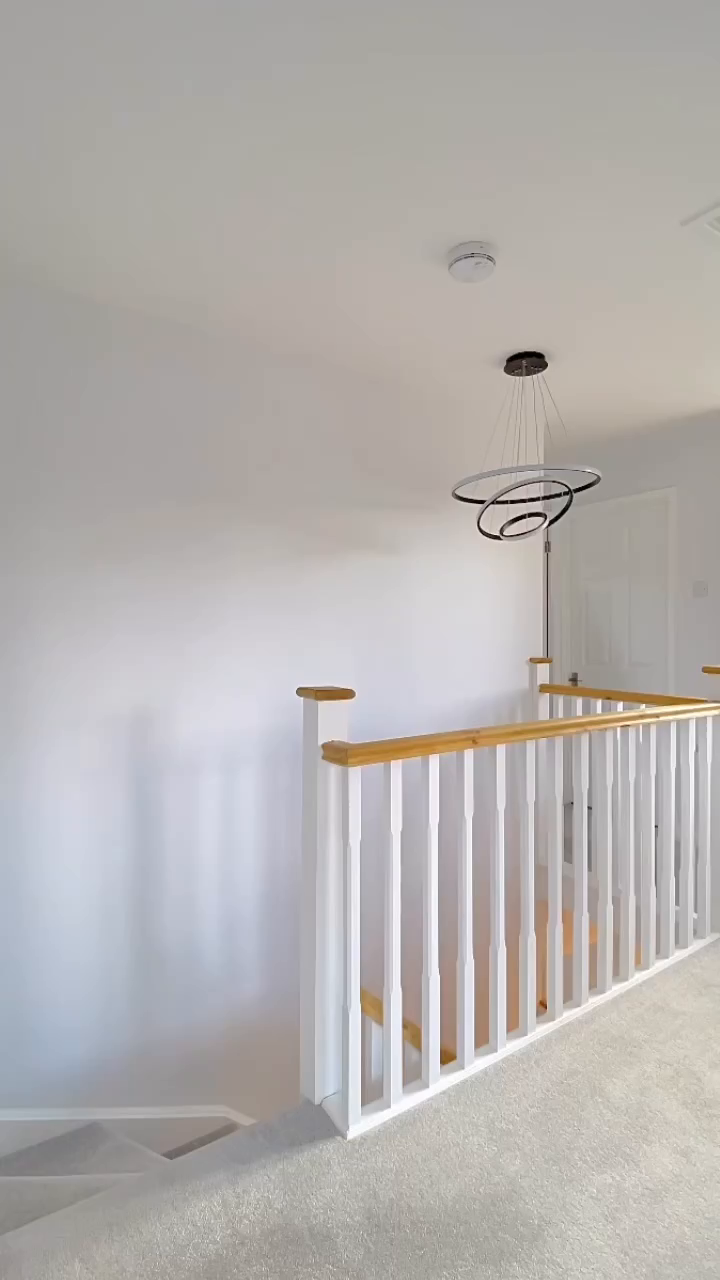 Corridoio con pareti bianche, scale rivestite di moquette e un moderno lampadario ad anello.