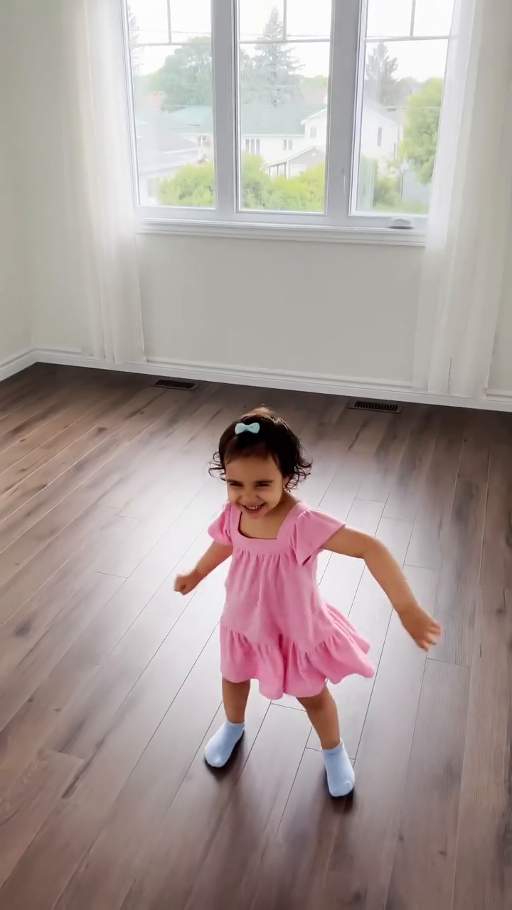 A young child in a pink dress dances on a wood floor.