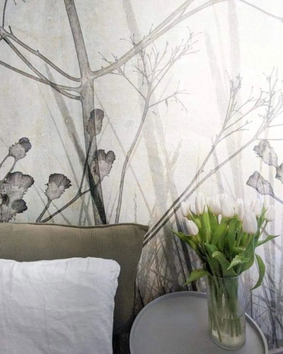 Detalle de dormitorio con tulipanes blancos en un jarrón, papel tapiz estampado y cama con almohada blanca.