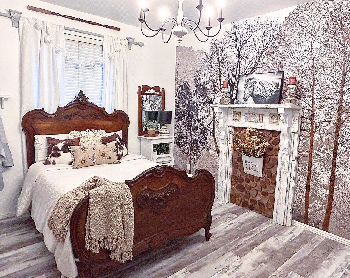 Bedroom with antique wood bed, white linens, and decorative pillows. Fireplace with horse art and tree wallpaper.