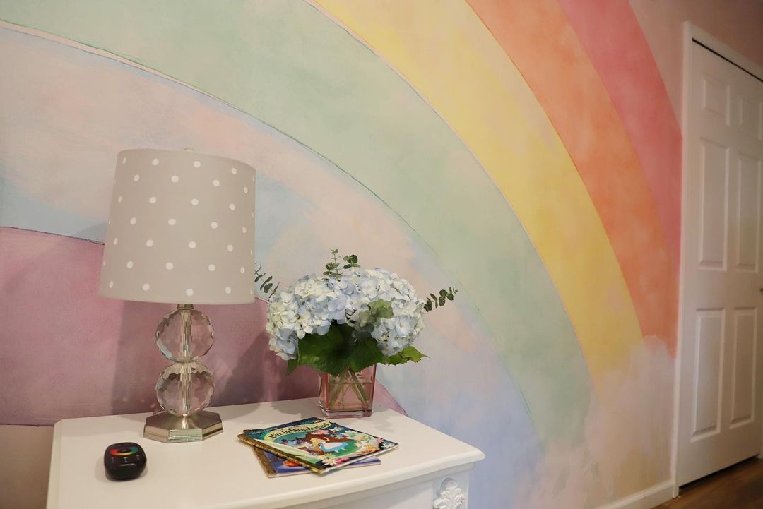 Kinderzimmer mit Regenbogenwand, gepunkteter Lampe und blauen Hortensien auf einer weißen Kommode.