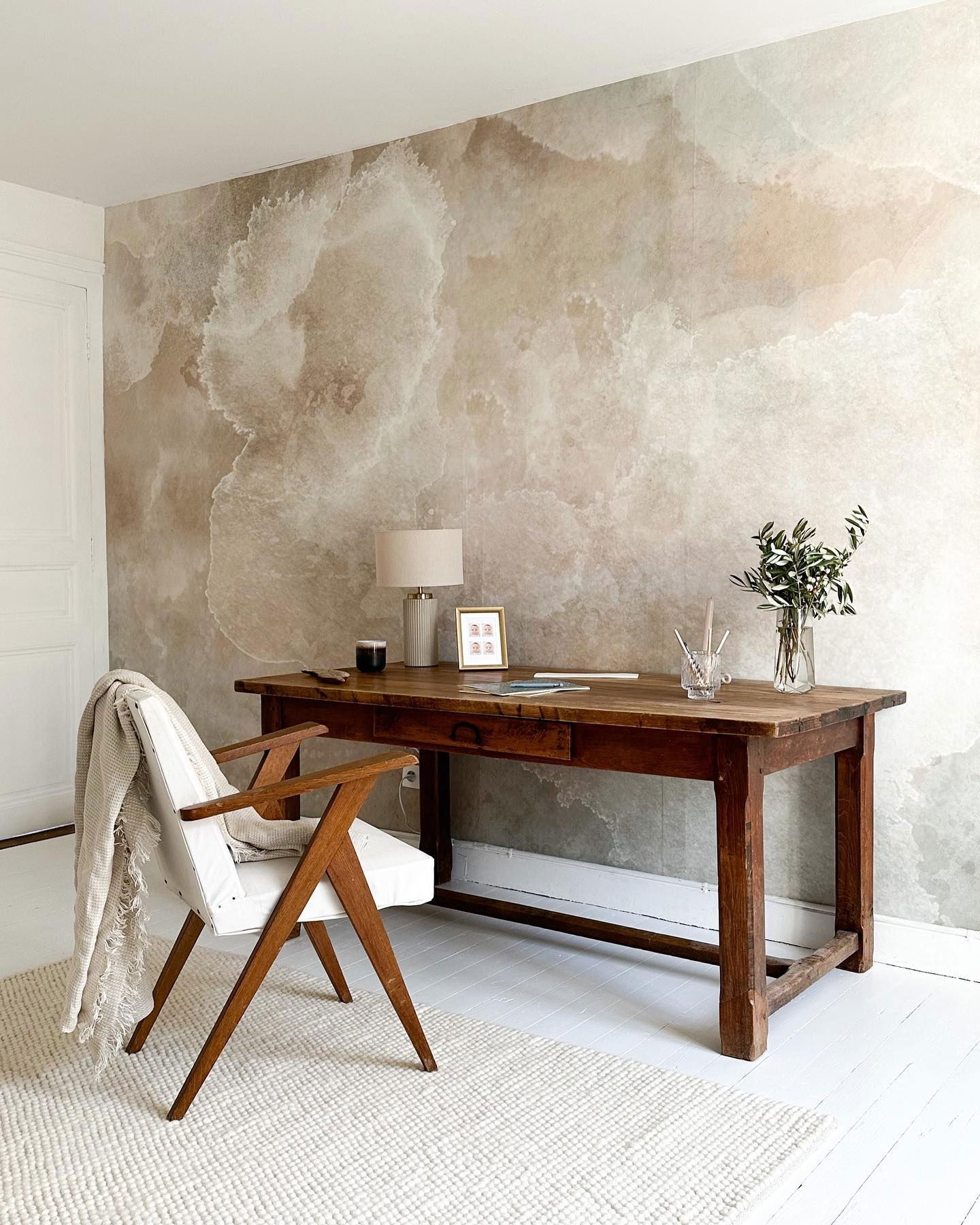 Oficina en casa con escritorio de madera, silla y papel tapiz con diseño de mármol.