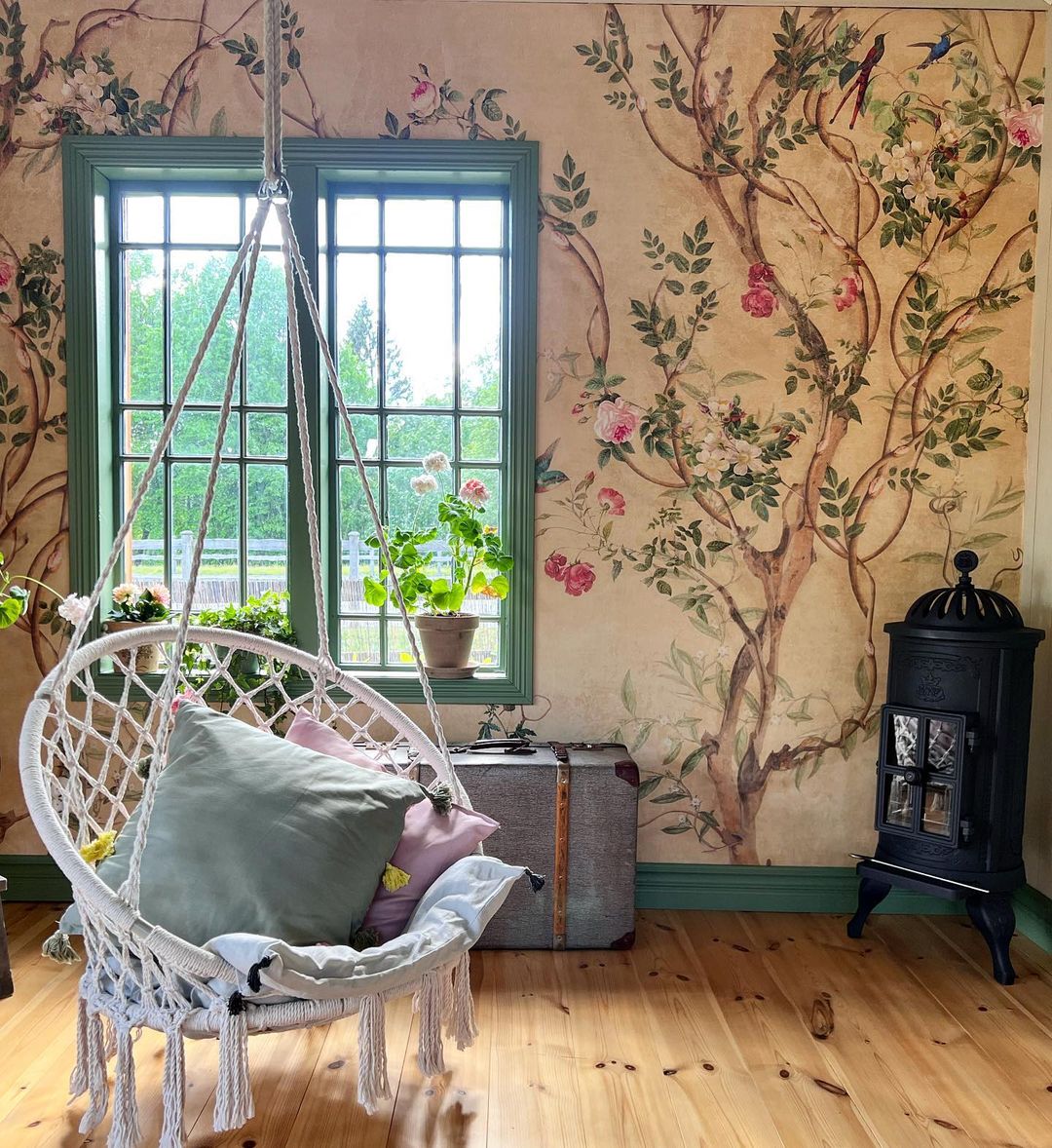 Hyggeligt værelse med blomstret tapet, hængende macrame stol med puder og en sort brændeovn.