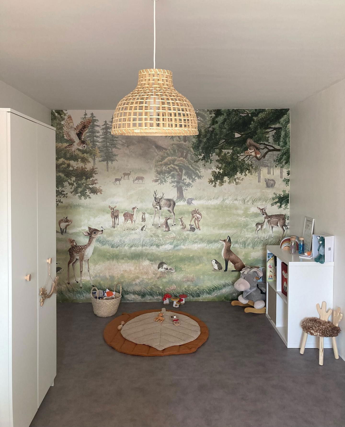 Chambre d'enfant avec une murale de forêt, une suspension tissée et un tapis en forme de feuille.