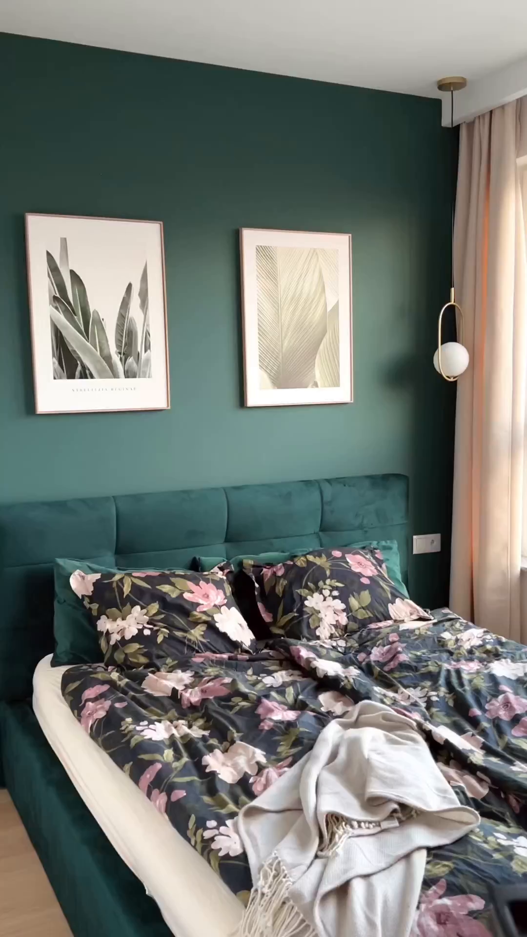 Bedroom with green walls, floral bedding, and botanical art prints.