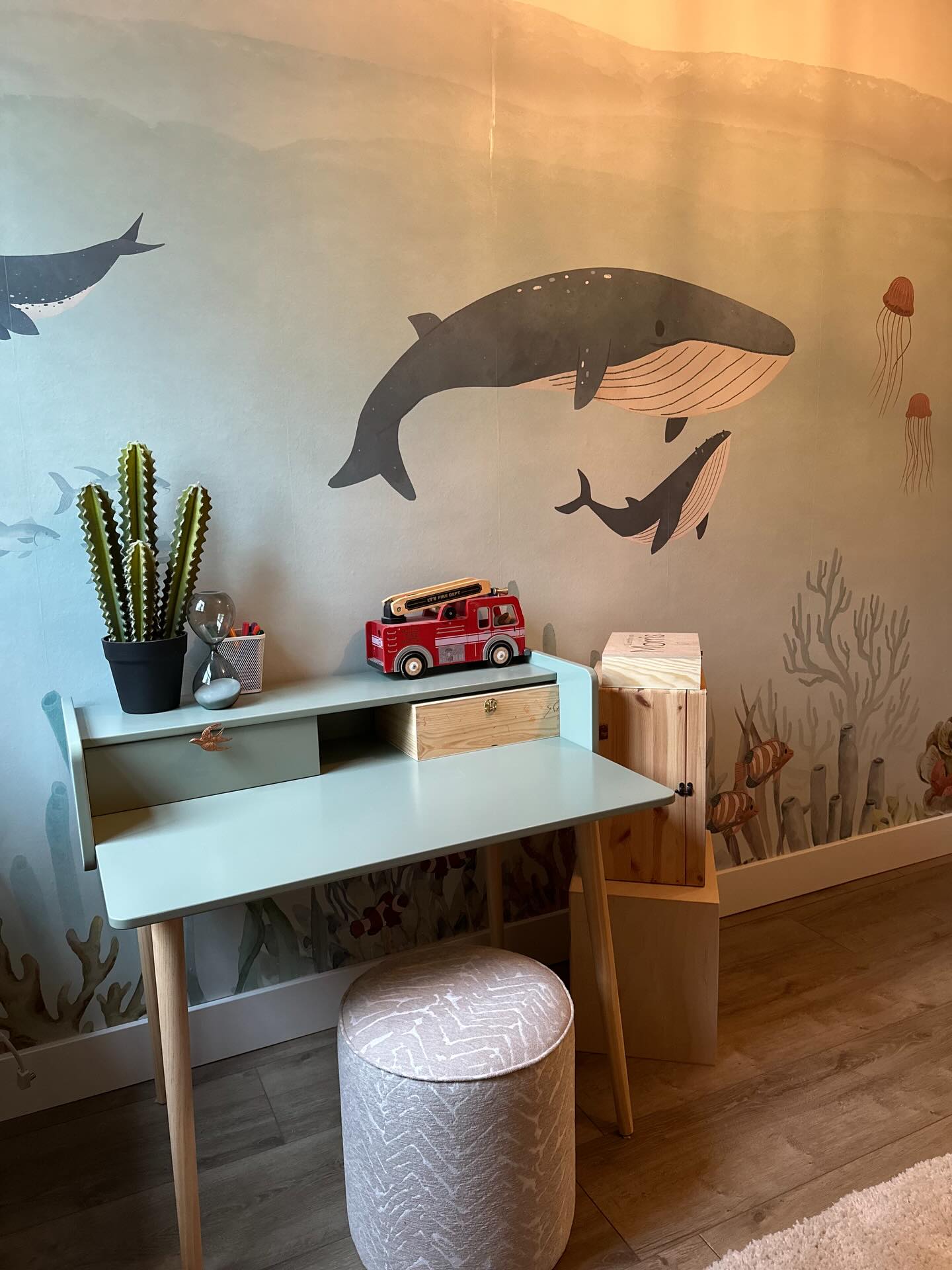Child's room featuring blue desk, patterned stool, and ocean-themed wallpaper with whales and jellyfish.