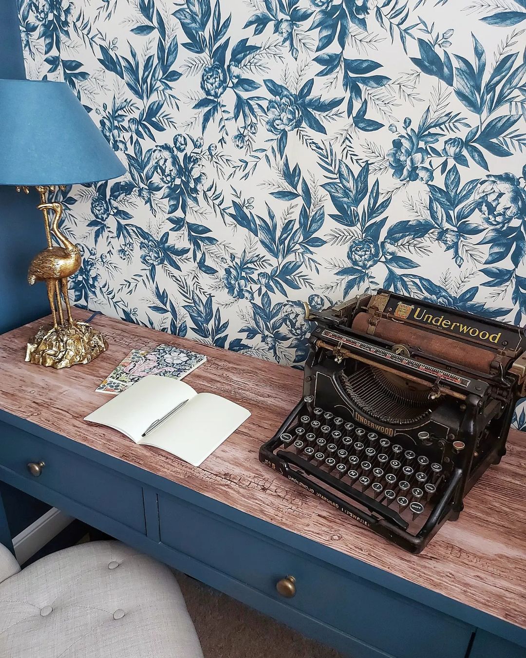 Vintage Underwood skrivemaskine på et blåt skrivebord med blomstret tapet.