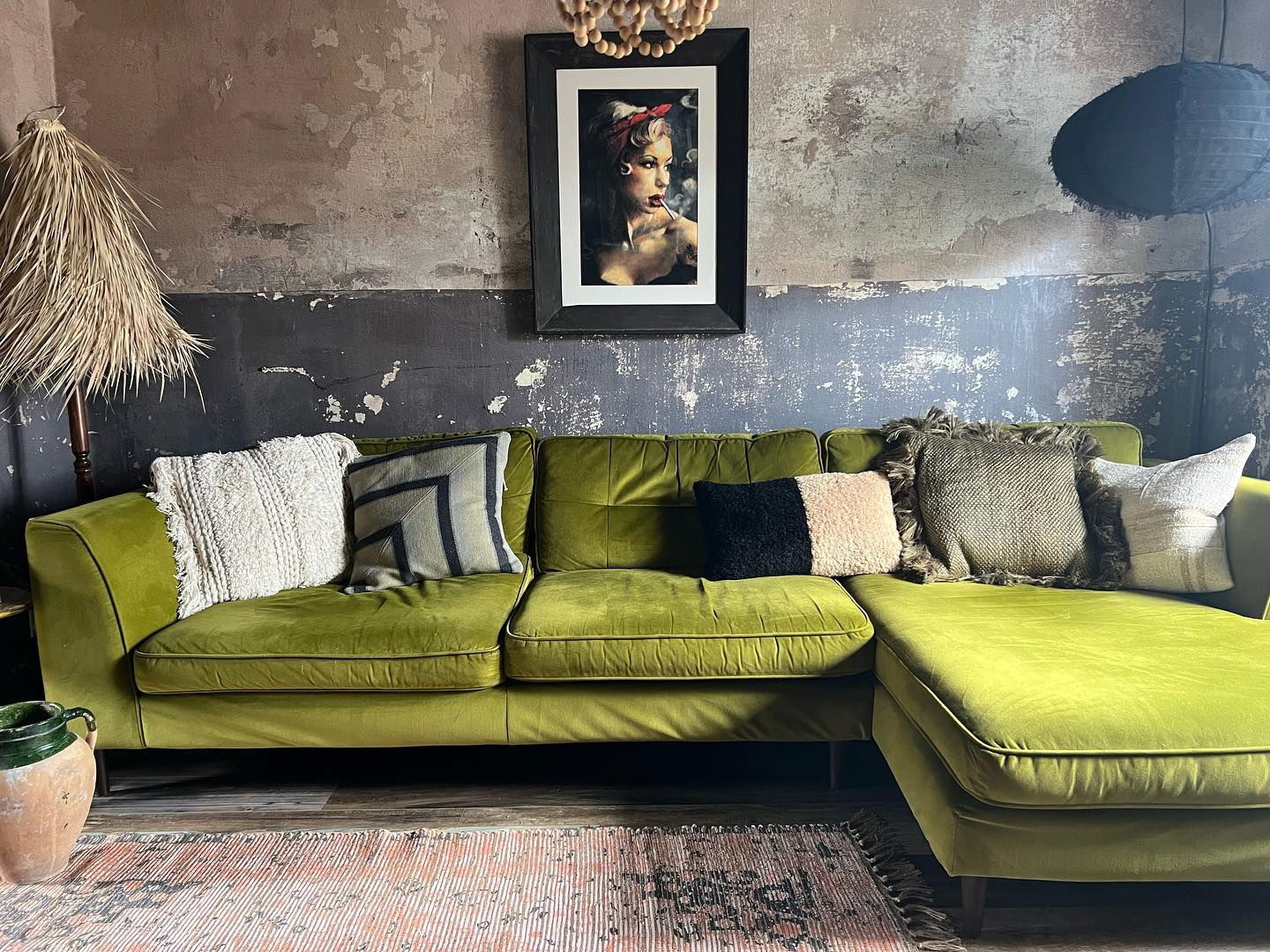 Living room with green velvet sofa, throw pillows, and framed art on a distressed wall.