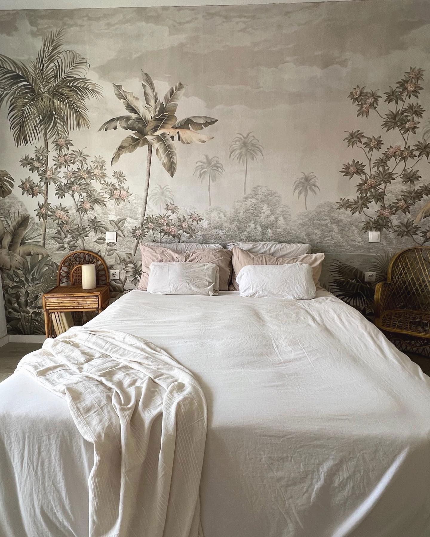 Bedroom with white linens, tropical mural, and rattan furniture.