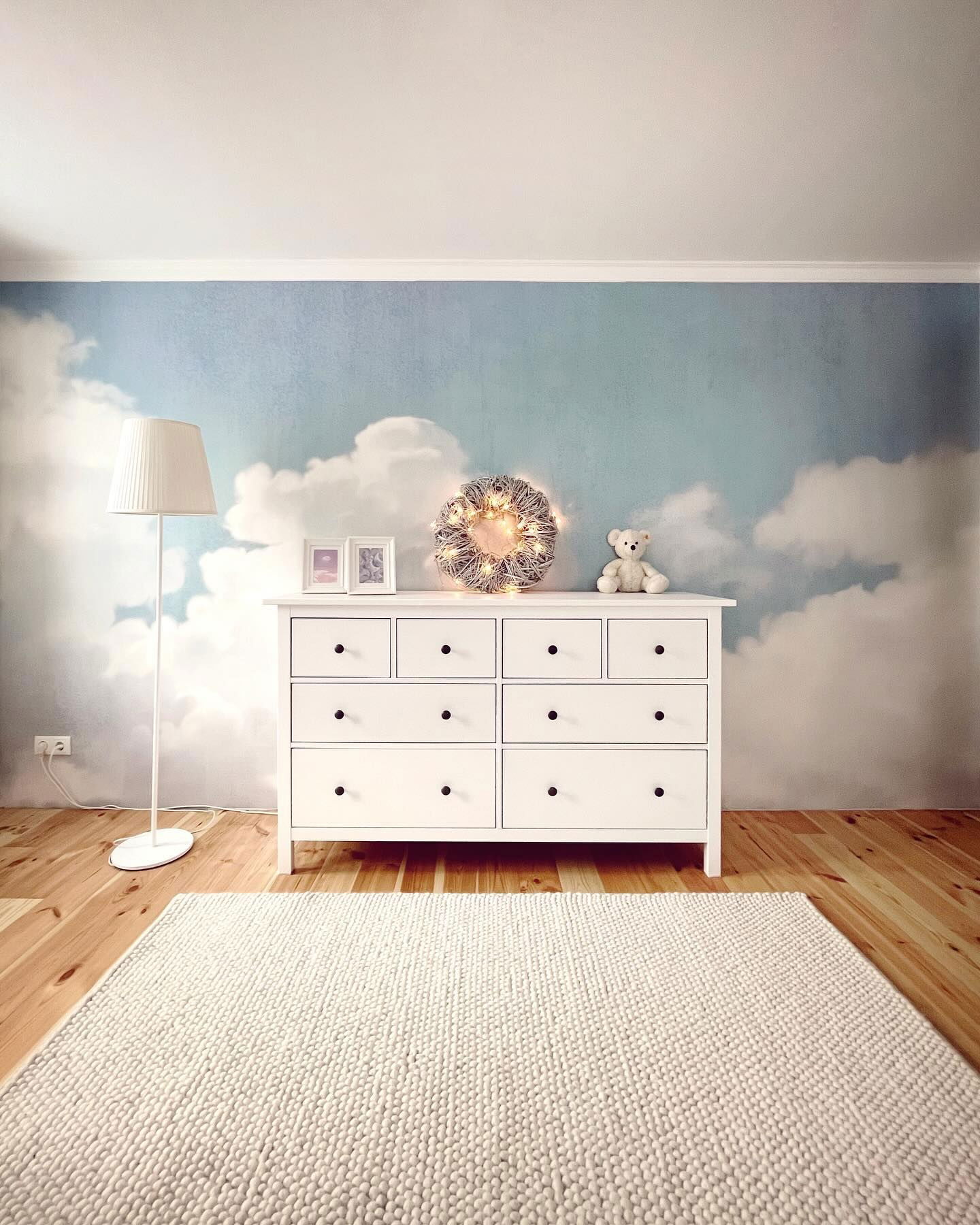 Nursery with white dresser against cloud wallpaper, white rug, and wood floor.